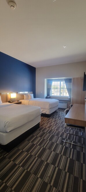 A hotel room with two beds, a desk, a chair, a TV, and a window with curtains. - Microtel Inn & Suites by Wyndham Fountain/Fort Carson (Fountain)