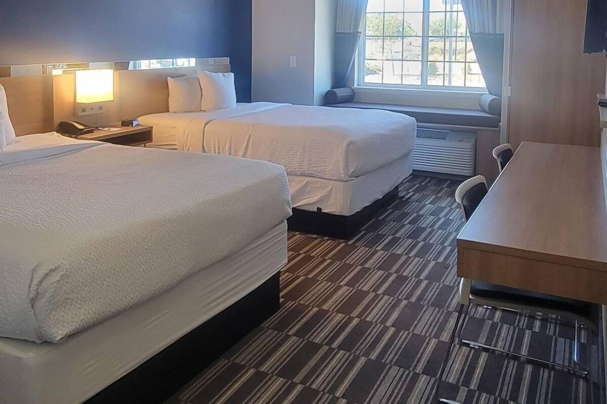A hotel room with two beds, a desk, a chair, a TV, and a window with curtains.
