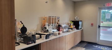 A breakfast bar with coffee machines, a waffle maker, and a juice dispenser.