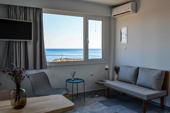 A modern room with a large window offering a view of the sea, a sofa, a small table, and a chair.
