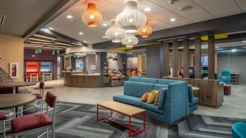 A modern lobby with a blue sofa, red chairs, a wooden reception desk, and pendant lighting.