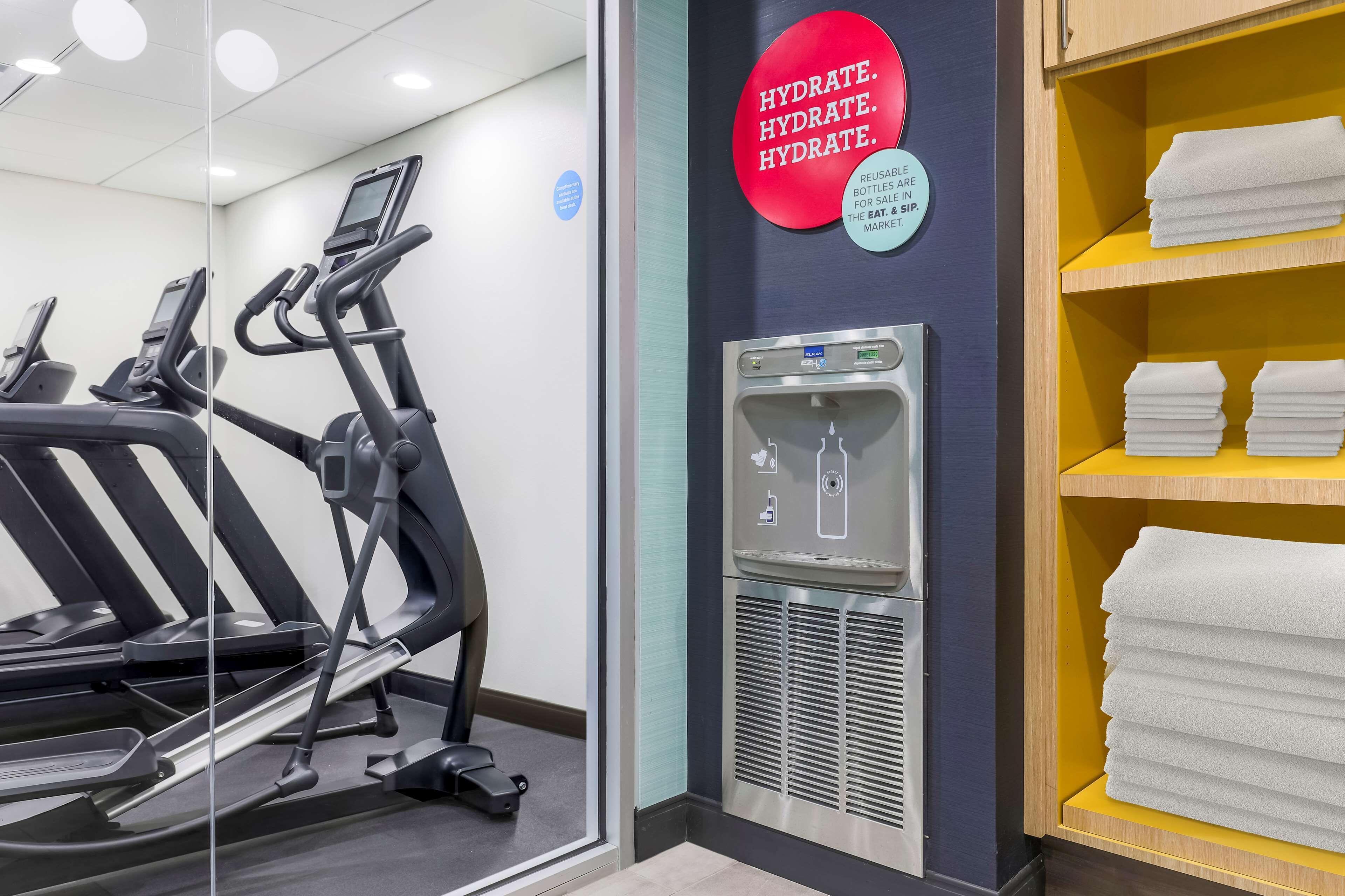Een fitnessruimte met loopbanden, een waterfontein en een plank met handdoeken.