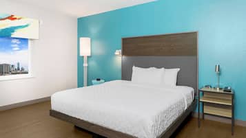 A modern hotel room with a large bed, a nightstand, a wall-mounted lamp, and a cityscape painting.