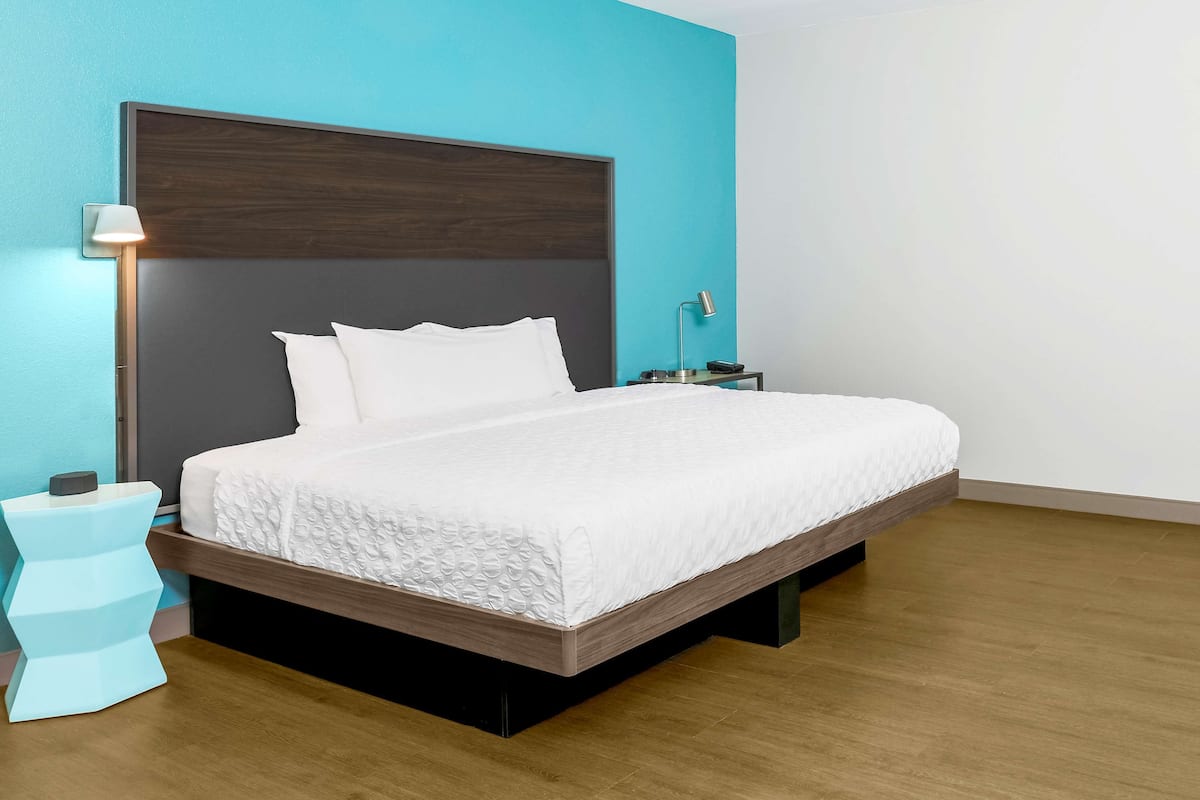A modern bedroom with a large bed, a nightstand, a lamp, and a wall-mounted shelf.