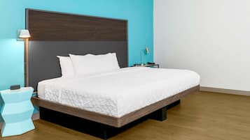 A modern bedroom with a large bed, a nightstand, a lamp, and a wall-mounted shelf.