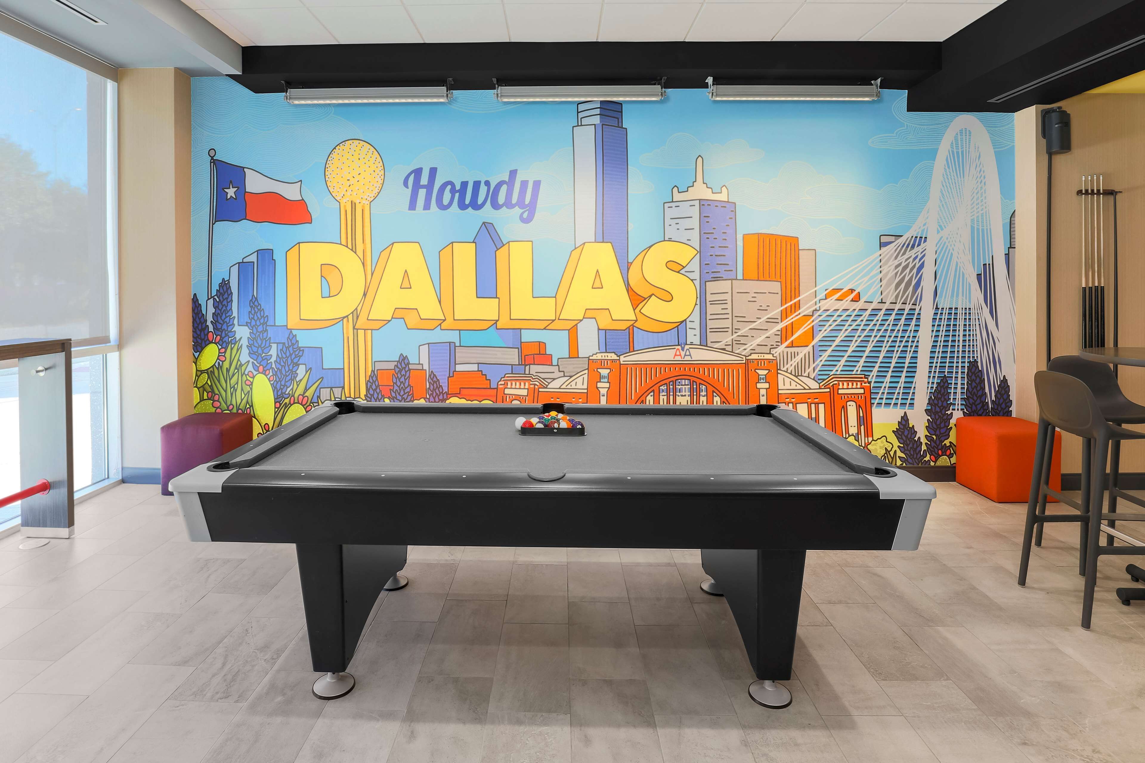 A pool table in a room with a mural of Dallas, Texas, and a bar area with stools.