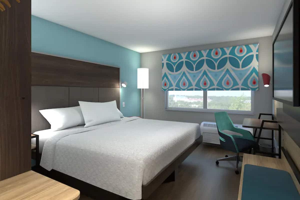 A hotel room with a bed, a desk, a chair, a TV, and a window with a view.