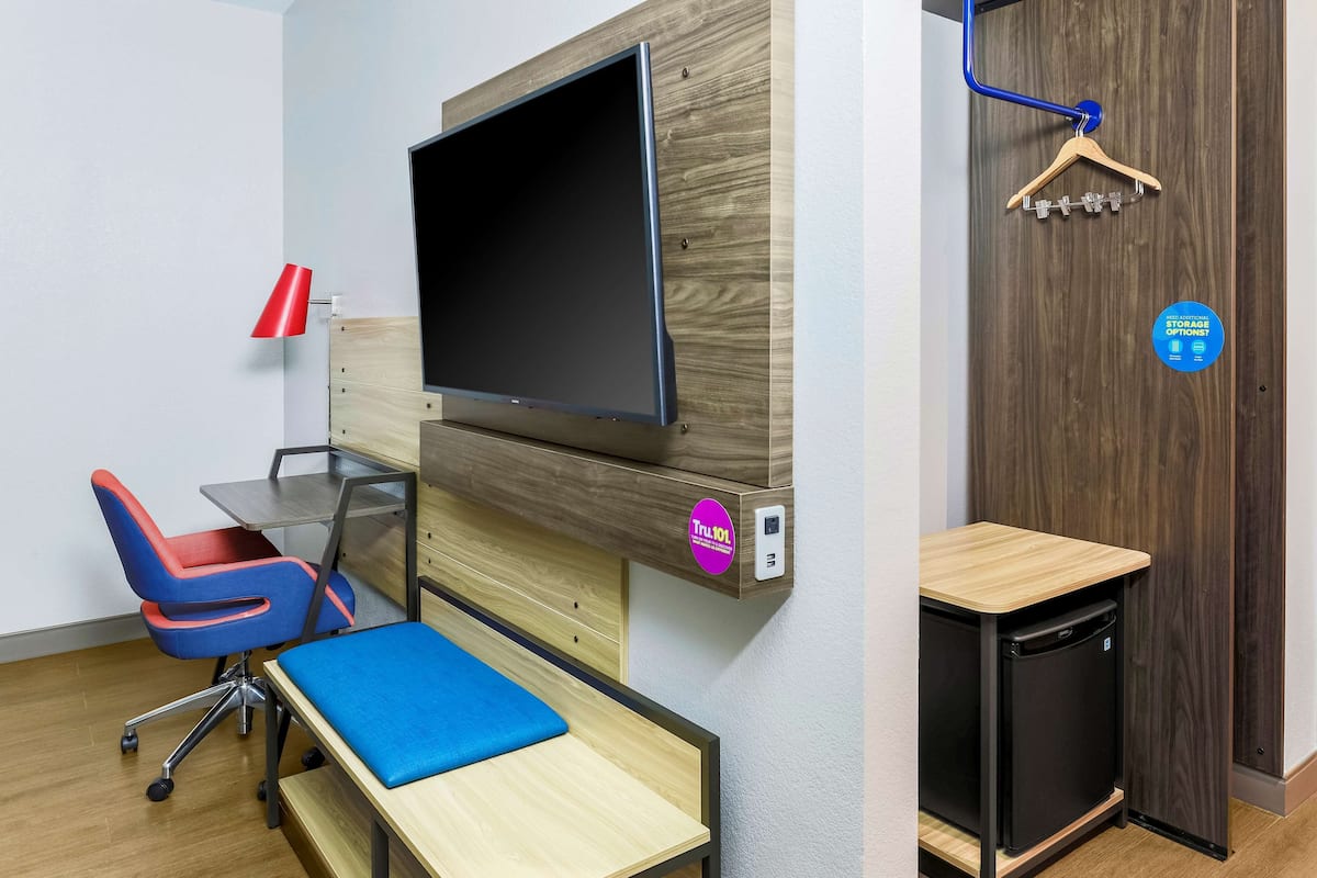 A modern office space with a flat-screen TV, a desk with a chair, a small refrigerator, and a coat rack.