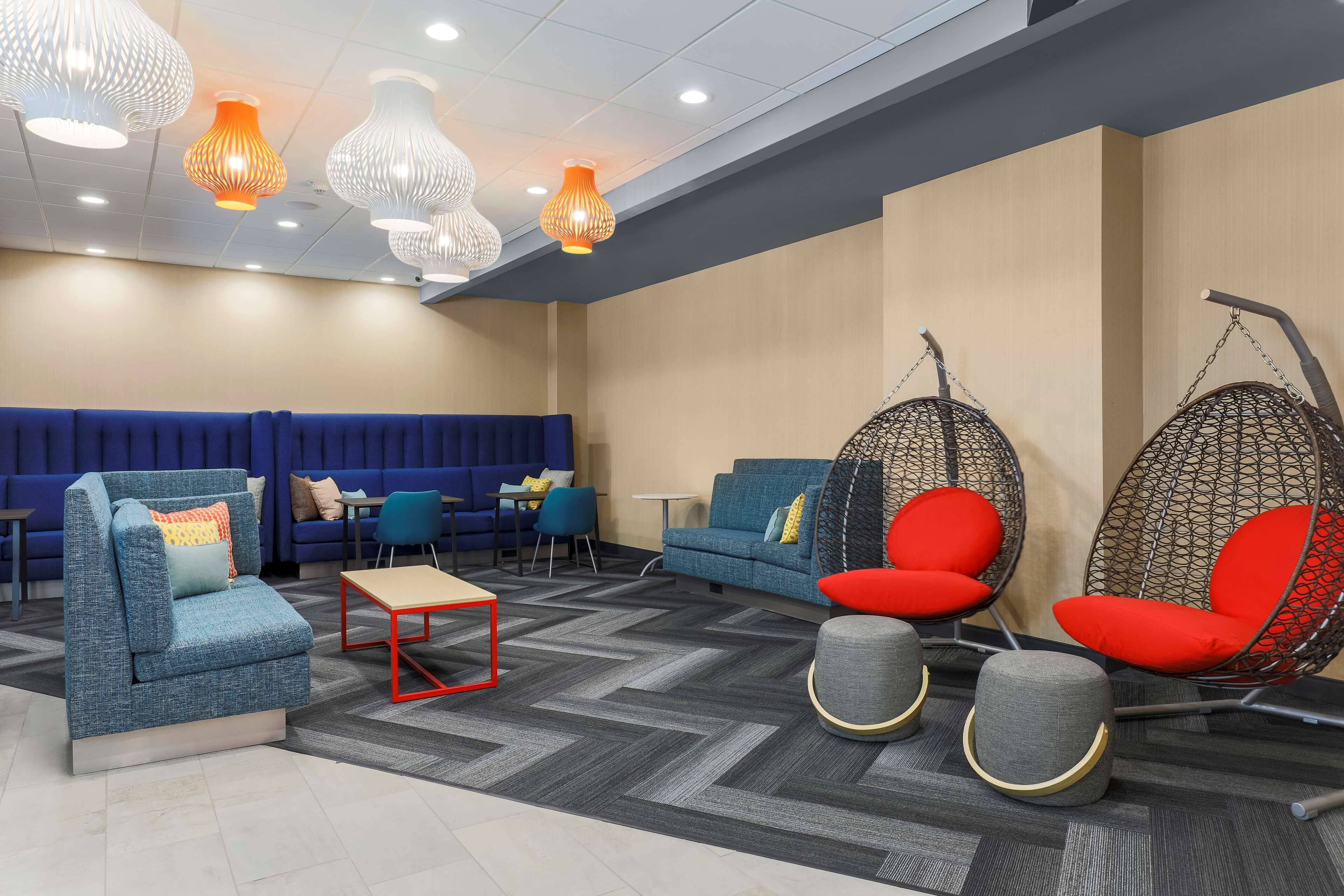 Un espace de détente moderne avec un canapé bleu, des fauteuils suspendus rouges et un tapis à motifs.