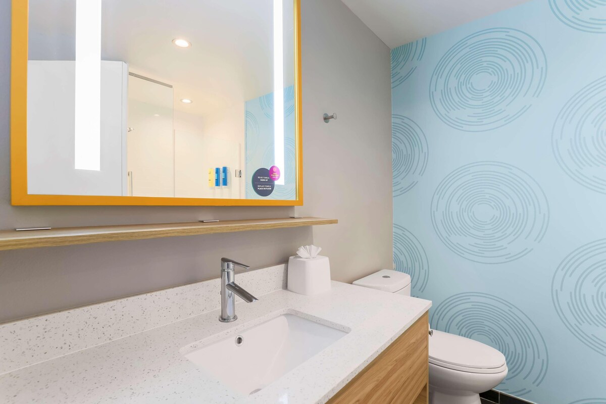 A modern bathroom with a white sink, a mirror with a yellow frame, a toilet, and a wall with circular patterns.