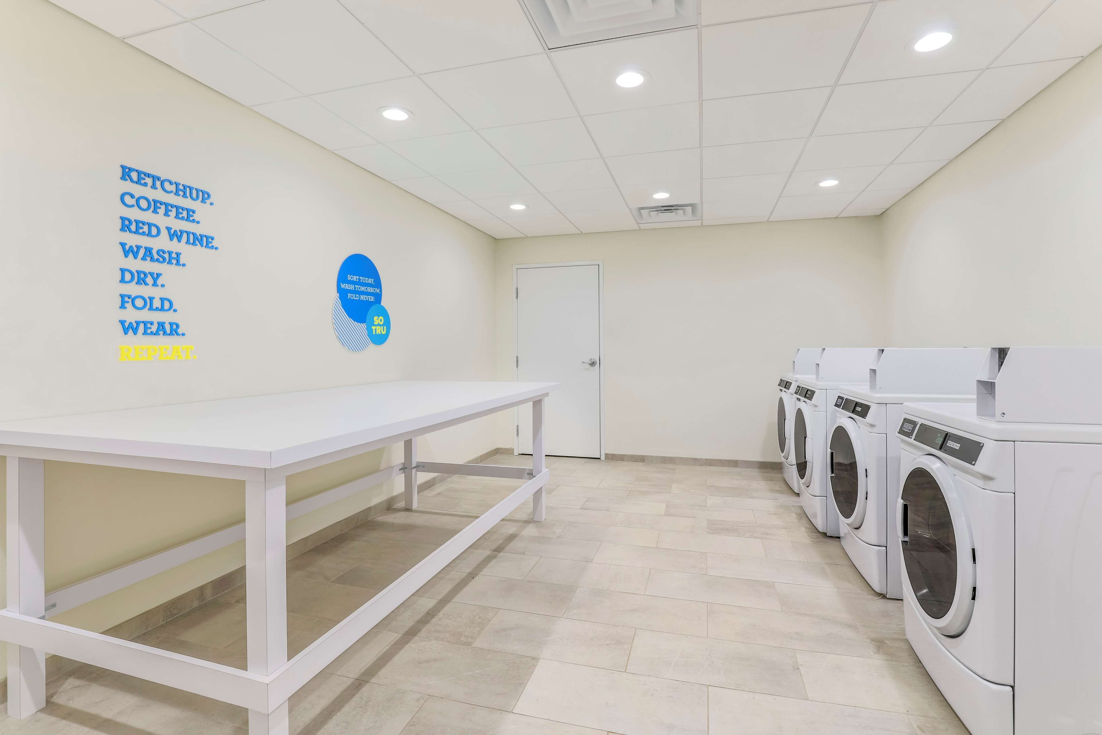 A laundry room with a white table, a wall-mounted sign, and a row of white washing machines.