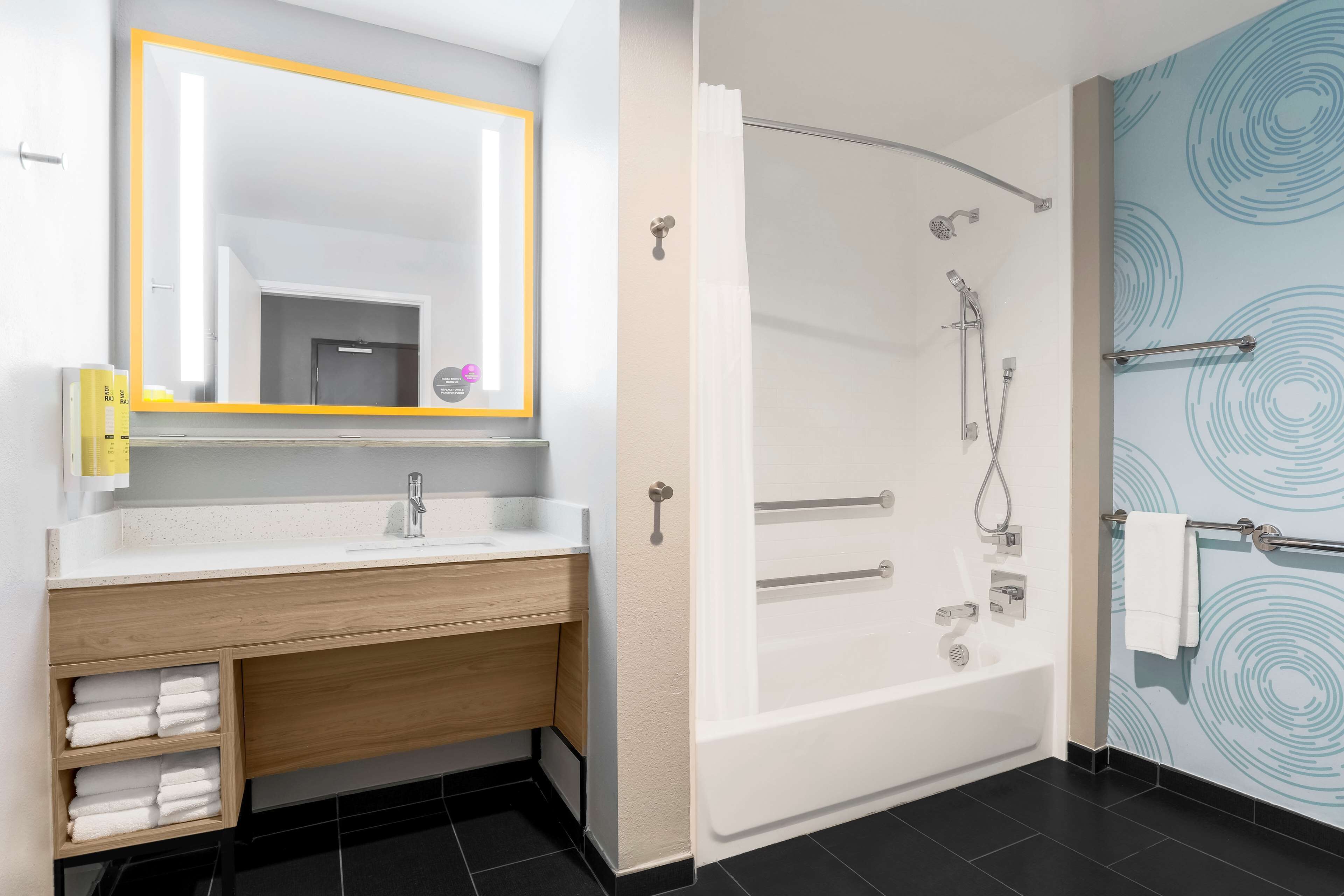 A modern bathroom with a wooden vanity, a large mirror, a bathtub, and a shower.