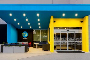 A modern hotel entrance with a blue and yellow facade, outdoor seating area, and a glass door entrance. - Tru by Hilton Dallas Downtown Market Center (Dallas)