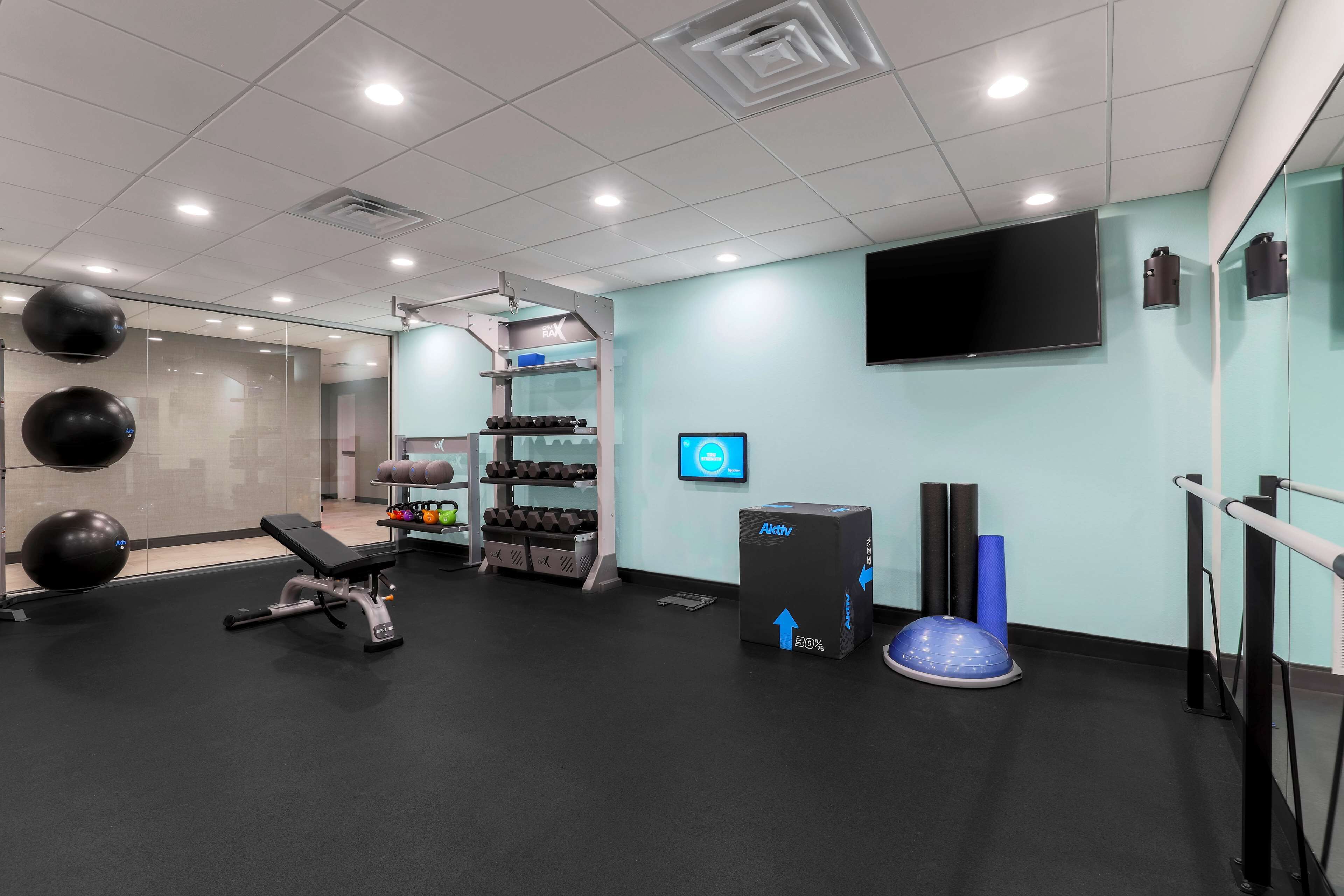 Un gimnasio moderno con equipamiento de ejercicio, una pantalla digital y un espejo grande.