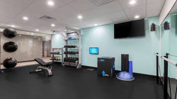 Un gimnasio moderno con equipamiento de ejercicio, una pantalla digital y un espejo grande.