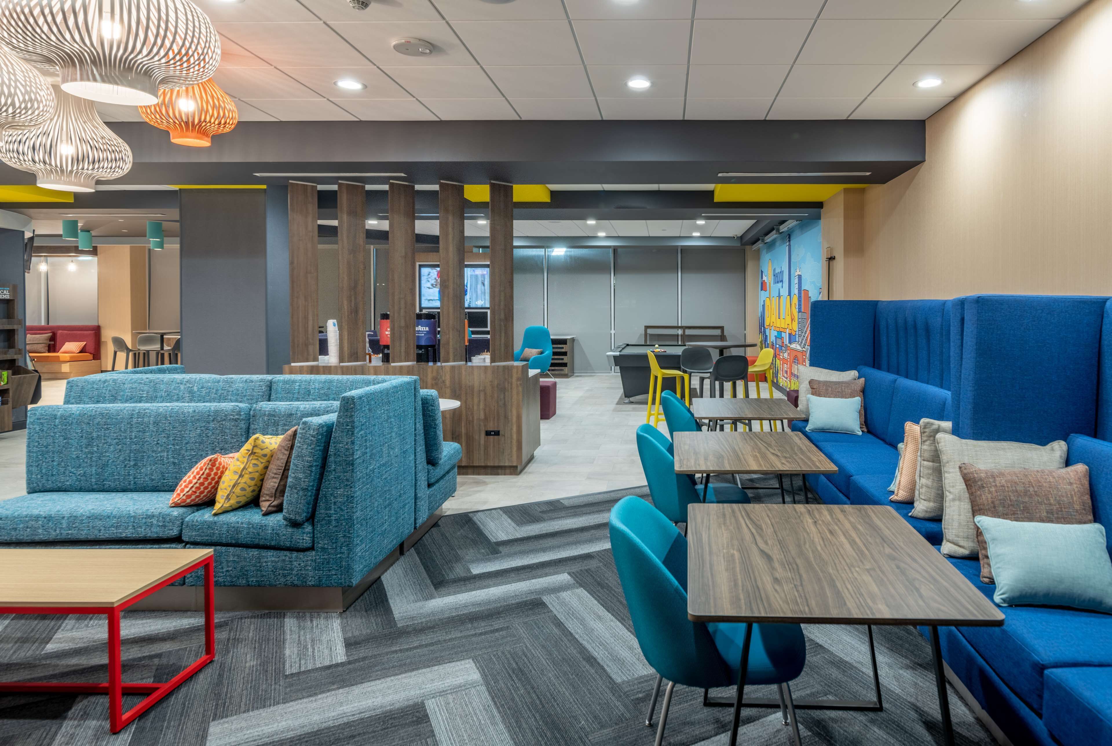 A modern lounge area with blue sofas, wooden tables, and colorful cushions.