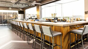 Zona de bar moderna amb una barra llarga, diversos tamborets i un gran finestral que ofereix una vista.
