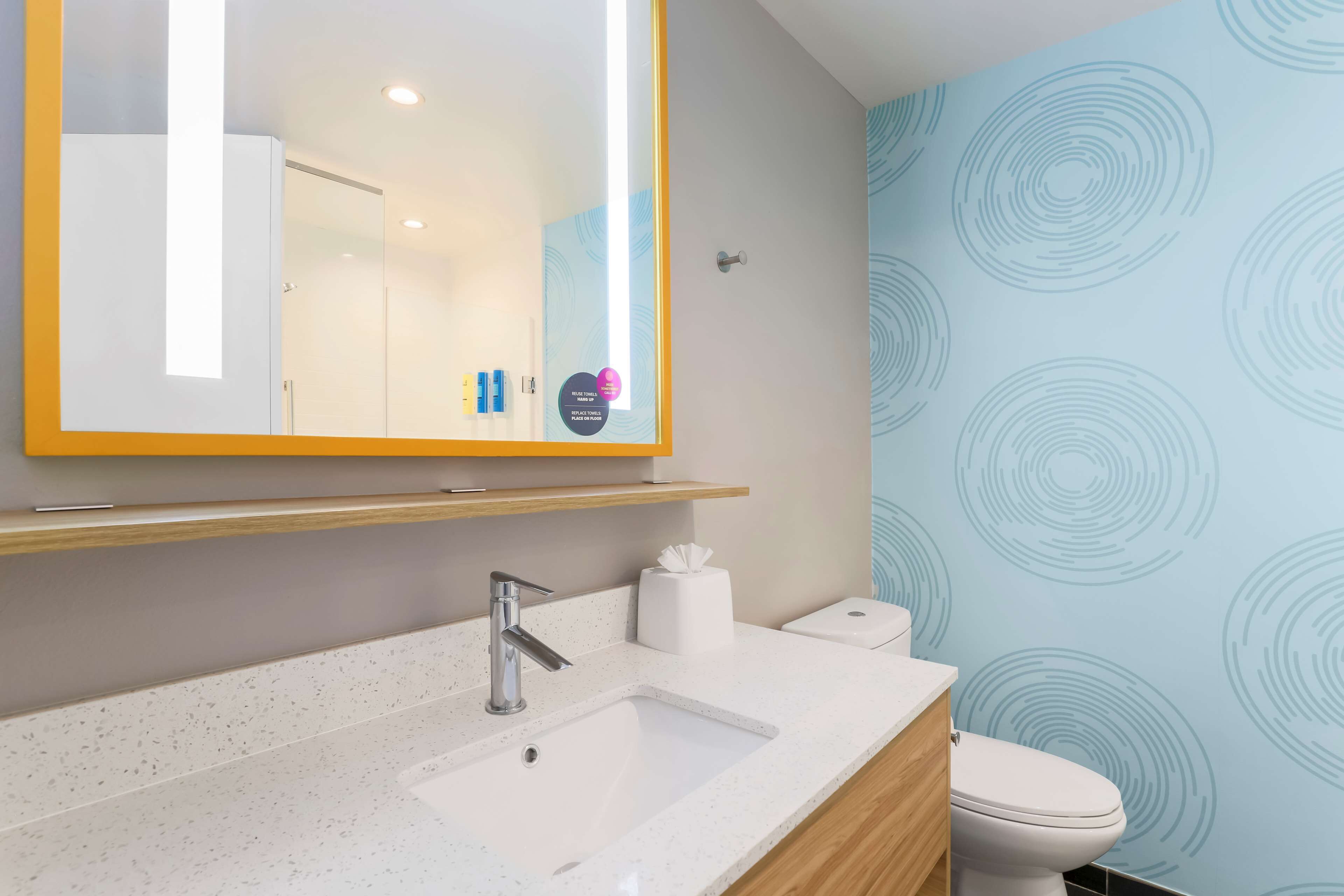 Een moderne badkamer met een witte wastafel, een spiegel met een gele omlijsting, een toilet en een muur met een rond patroon.