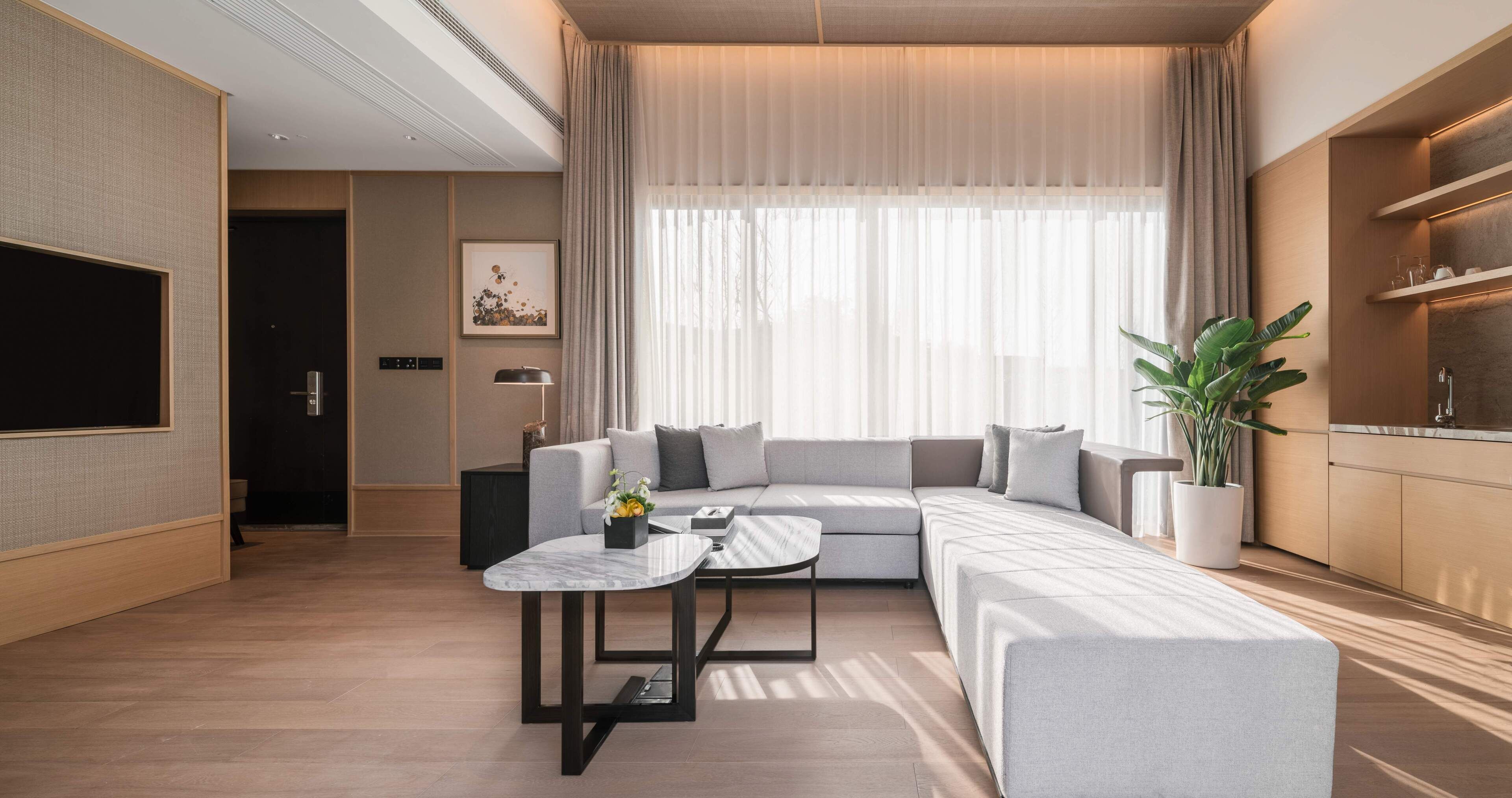 Una sala de estar moderna con un sofá modular, una mesa de centro, un televisor y una cocina con una planta.