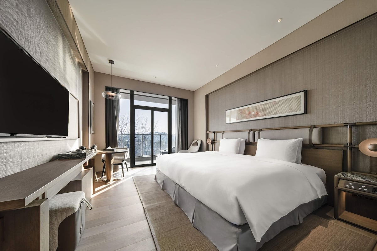 A modern hotel room with a large bed, a desk, and a TV.