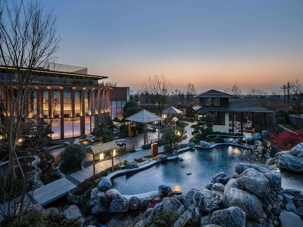 A modern building with large windows and a swimming pool surrounded by rocks and plants.