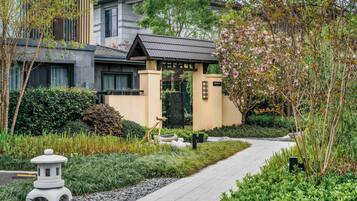 A modern residential building with a pathway, greenery, and a traditional stone lantern.