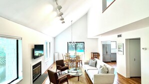 A modern living room with a fireplace, dining area, and kitchen. - Modern East Hampton Oasis – Heated Pool & Just Steps to Village (East Hampton)
