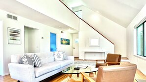 A modern living room with a sofa, armchair, coffee table, and a staircase leading to another level. - Modern East Hampton Oasis – Heated Pool & Just Steps to Village (East Hampton)