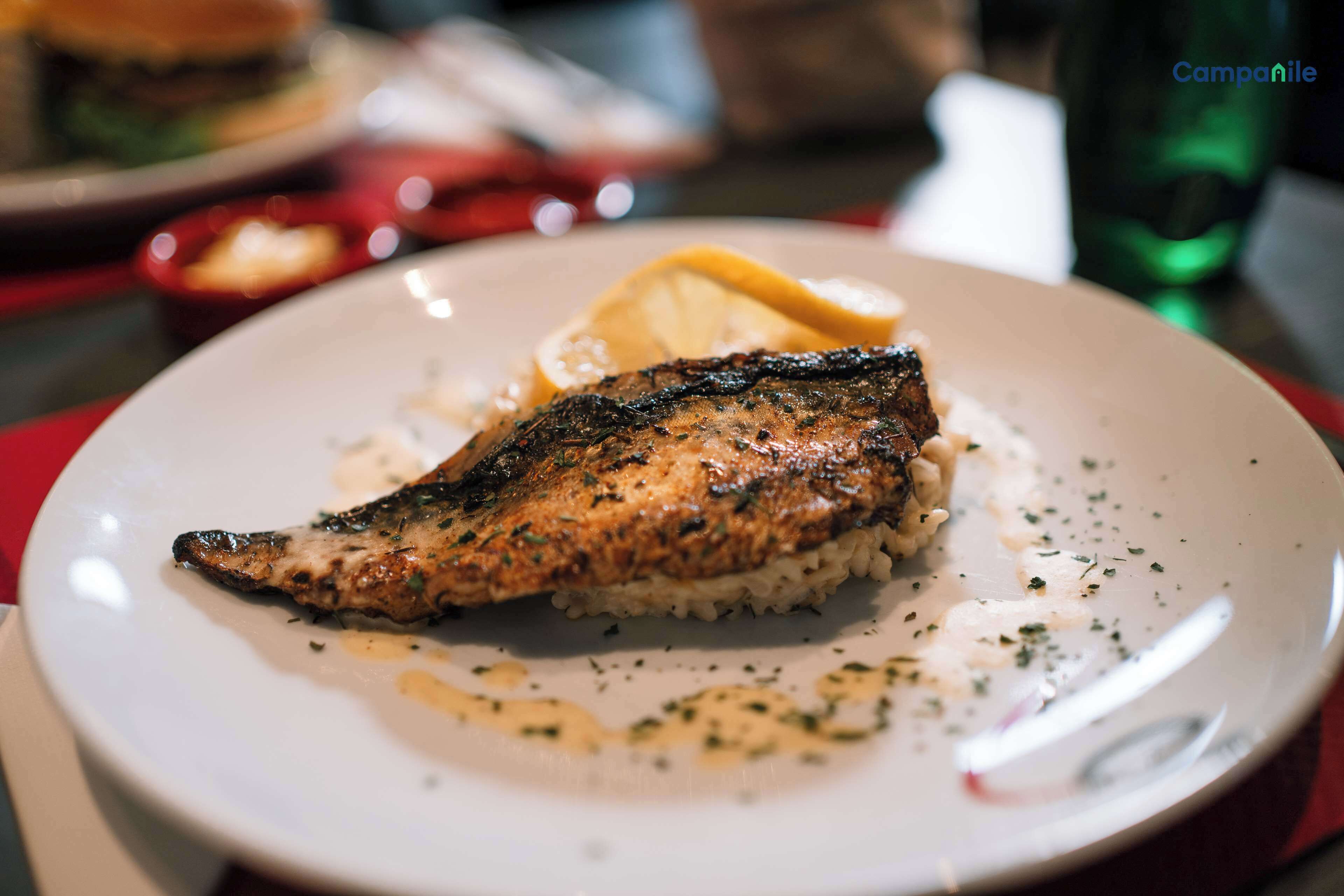 Une assiette contenant du poisson grillé, du riz et un quartier de citron, posée sur une table.