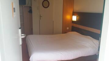 A hotel room with a bed, a wardrobe, and a wall-mounted light.