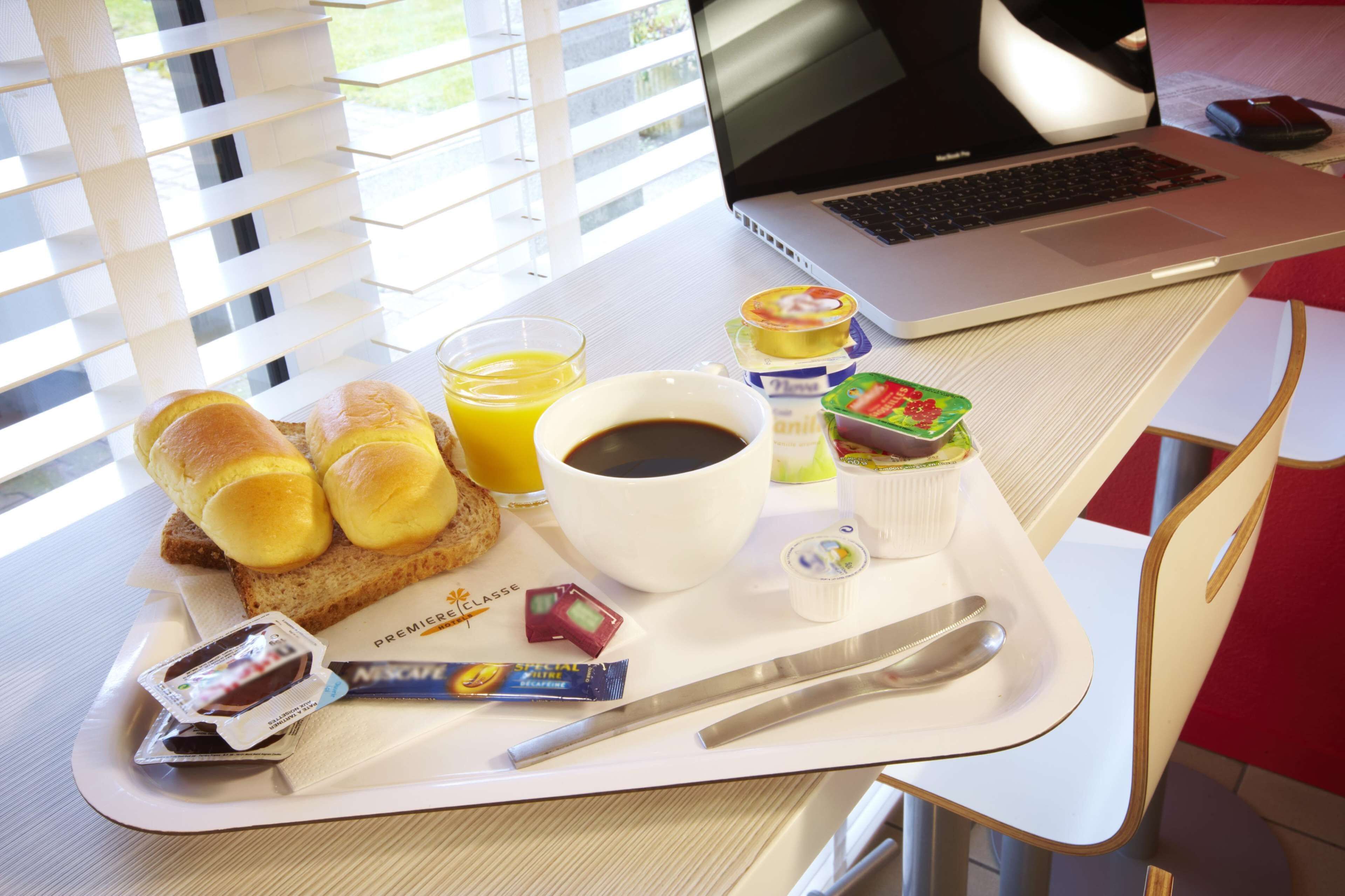 Bandeja de desayuno con pan, jugo, café, yogur y una computadora portátil sobre una mesa.