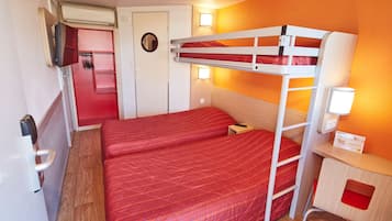 A bunk bed room with a red bedspread, a small desk with a lamp, and a door with a mirror.