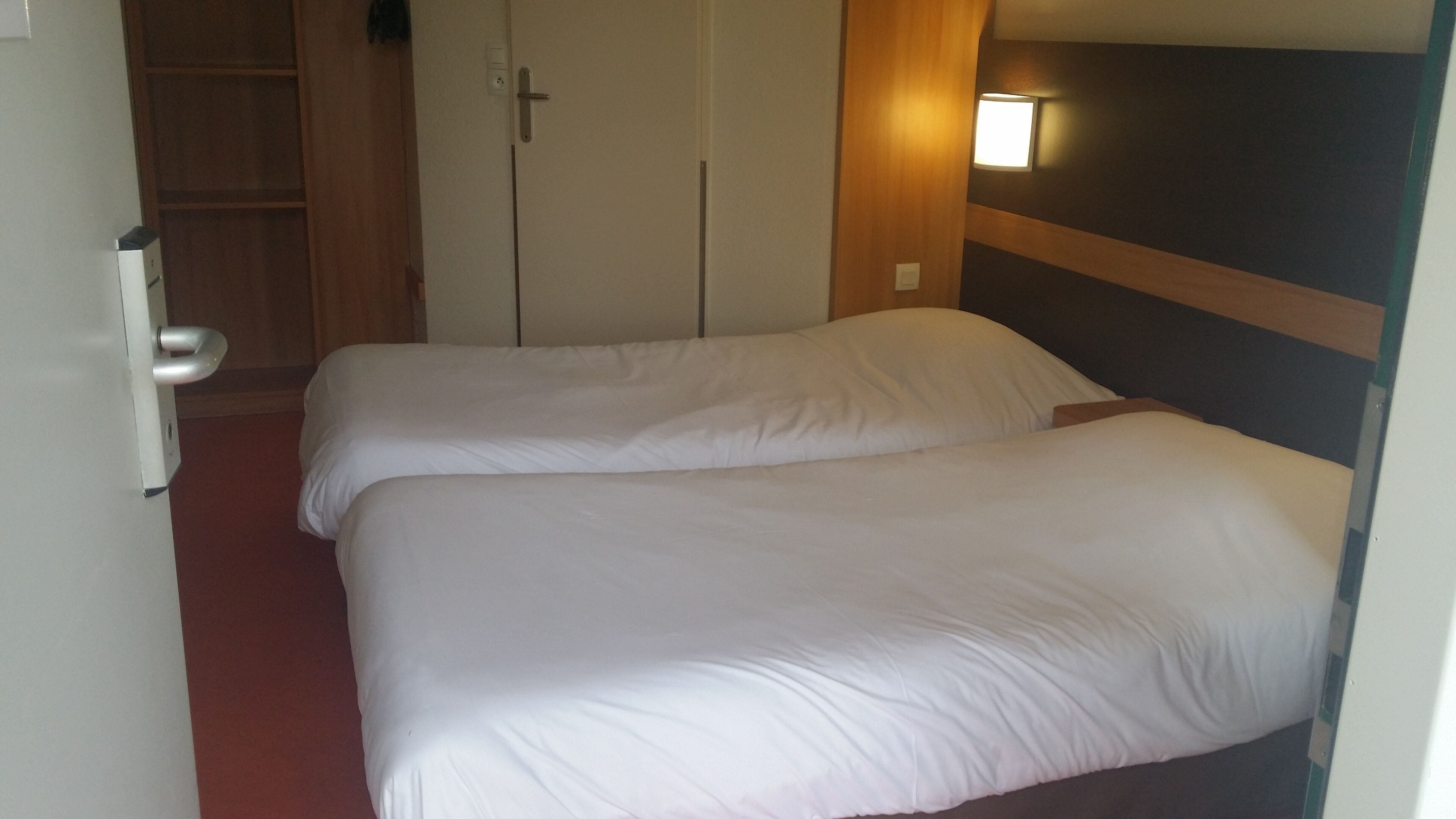 Una habitación de hotel con dos camas individuales, un armario de madera y una lámpara fijada a la pared.