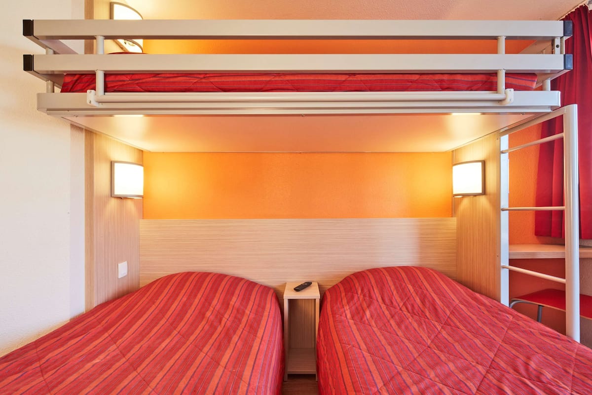 Een slaapkamer met een stapelbed, een klein tafeltje en een rood gordijn.