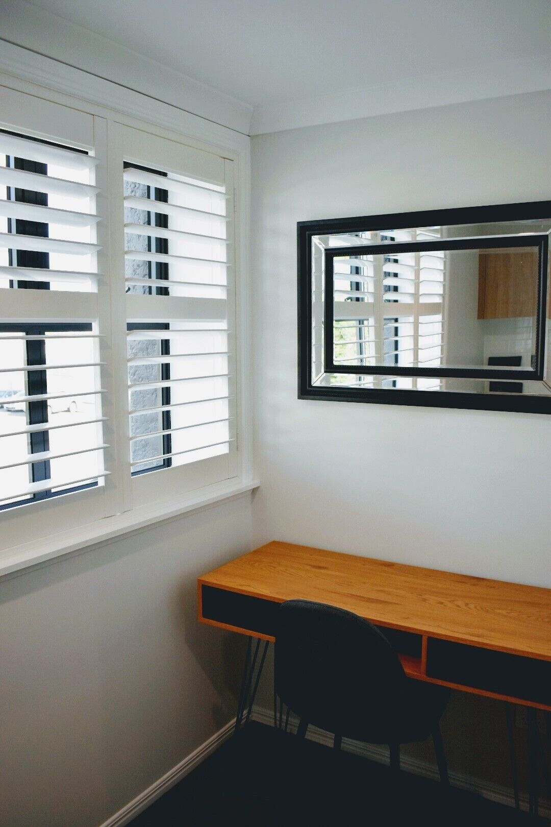 A room with a desk, a chair, a window with blinds, and a mirror on the wall.