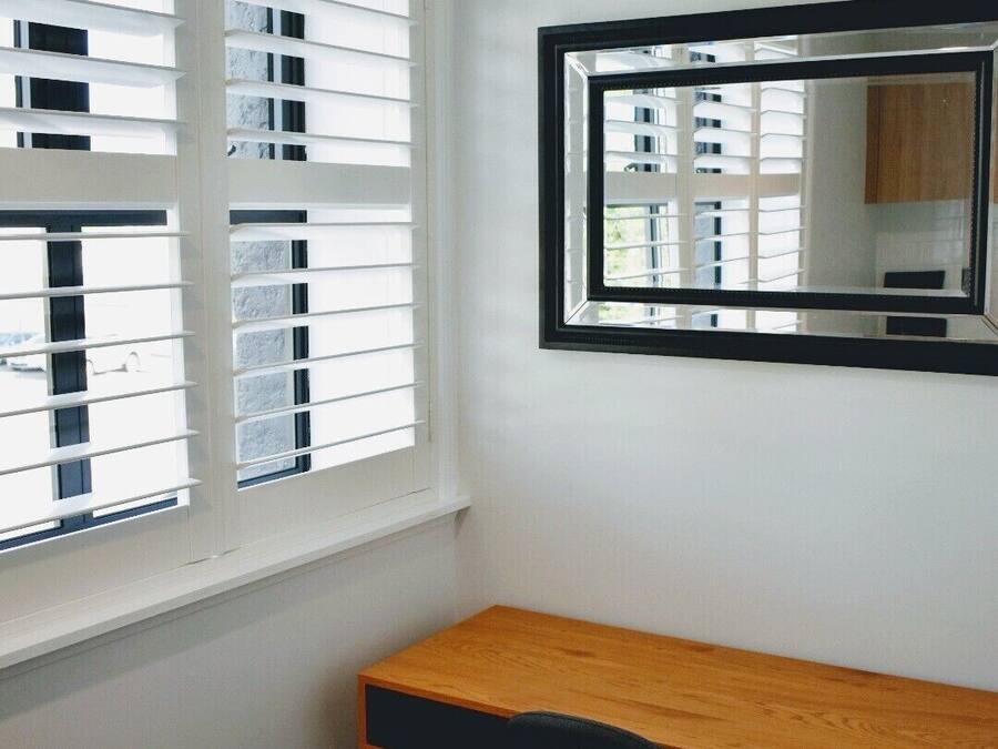 A room with a desk, a chair, a window with blinds, and a mirror on the wall.