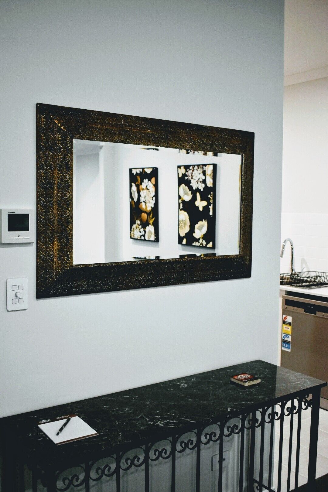 Un bagno con un lavabo bianco, un piano d'appoggio in marmo nero e uno specchio con decorazioni floreali.
