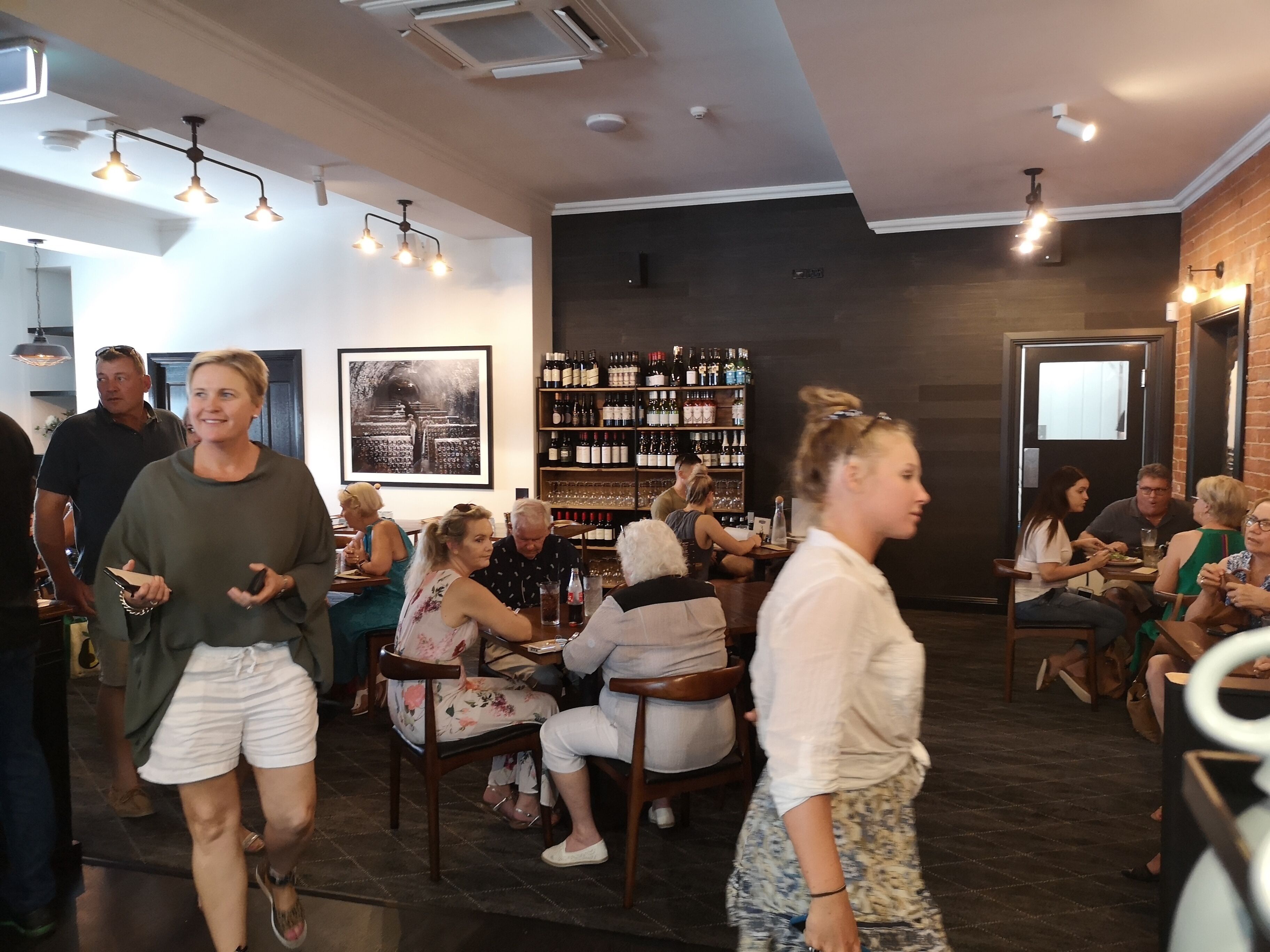 L’intérieur d’un restaurant, avec un bar, des tables et des chaises, et un présentoir à vin.