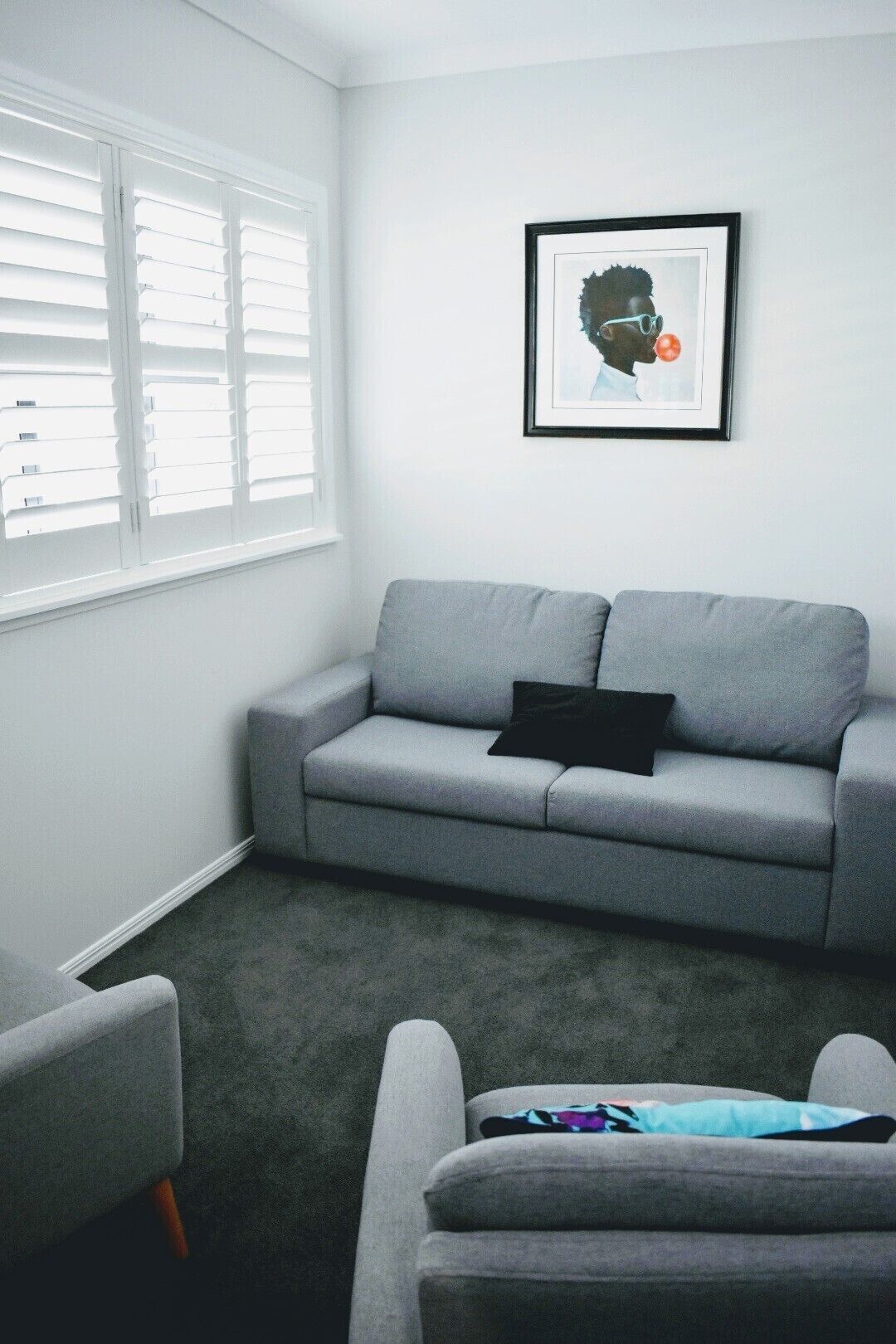 Ein Wohnzimmer mit grauem Sofa, einem schwarzen Kissen und einem gerahmten Bild an der Wand.