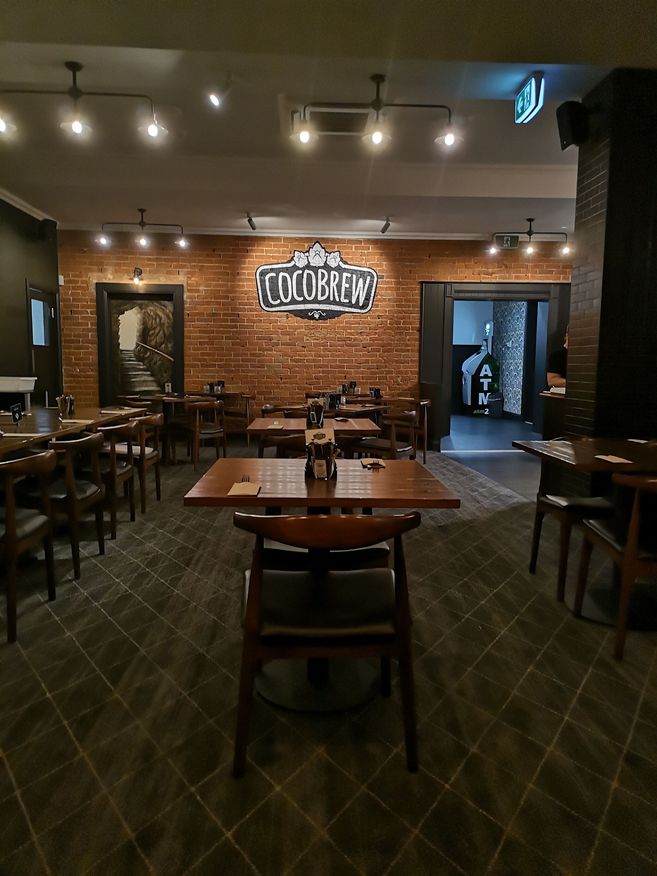 A restaurant interior with brick walls, wooden tables and chairs, and a sign reading "COCOBREW".