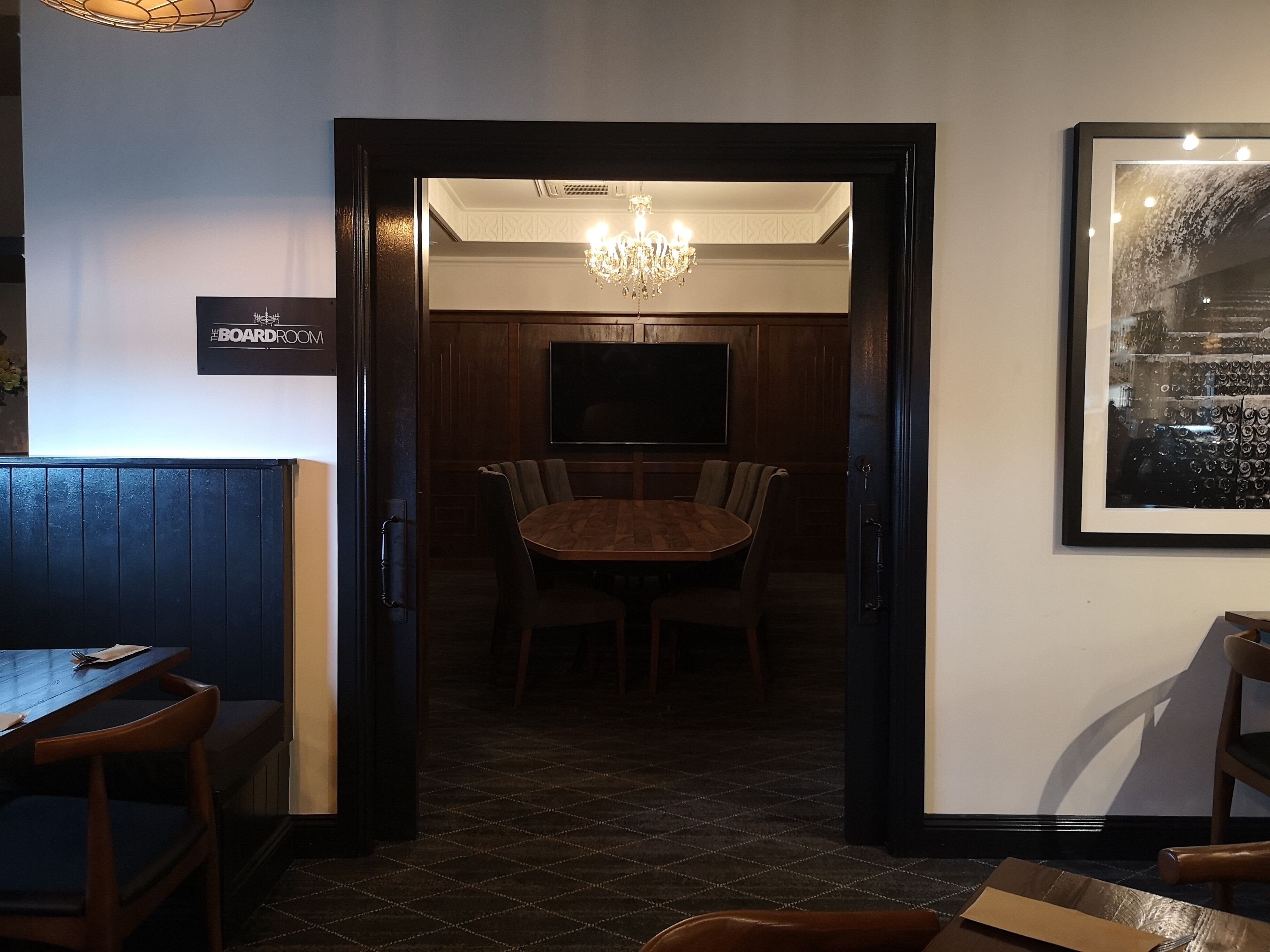 A dining area with a wooden table and chairs, a chandelier, and a television mounted on the wall.