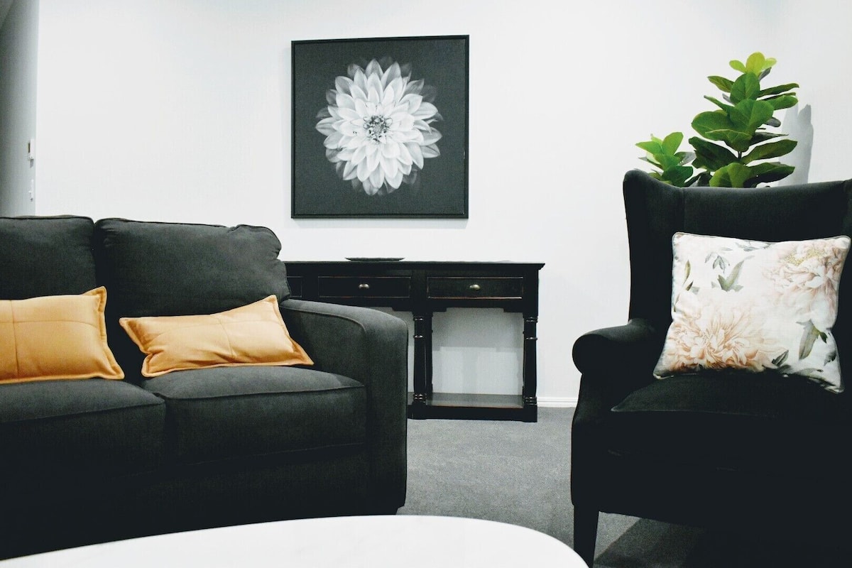 A living room with a dark sofa, a small side table, and a chair with a floral cushion.
