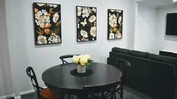 Un coin repas avec une table ronde, des chaises et un vase de fleurs. Trois tableaux sont accrochés au mur au-dessus de la table.