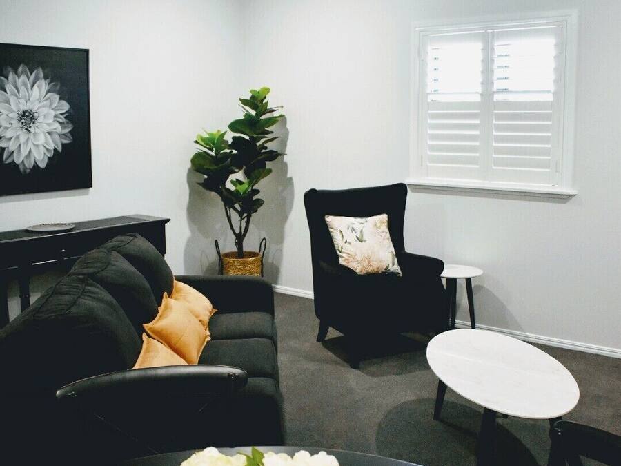 A modern living room with a black sofa, a black armchair, a small round table, and a white vase with flowers.