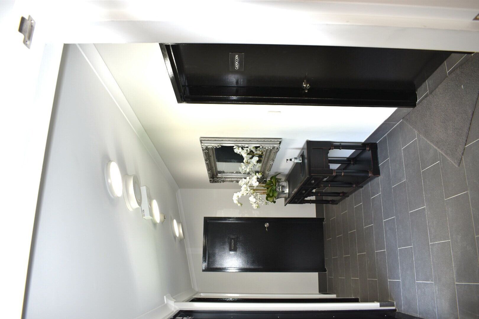 A modern bathroom with a black bathtub, a mirror above the sink, and a small white flower arrangement.