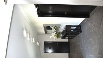 A modern bathroom with a black bathtub, a mirror above the sink, and a small white flower arrangement.