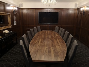 A conference room with a large wooden table, eight grey upholstered chairs, a flat-screen TV, a chandelier, and a decorative mirror. - CocoBrew Boutique Apartments (Rockhampton)