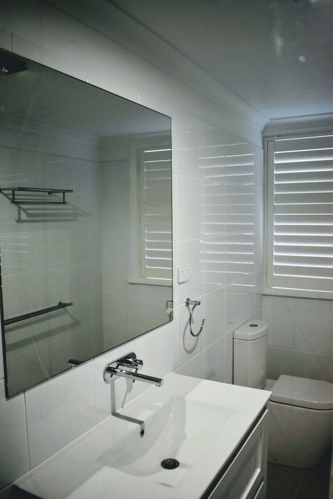 Une salle de bain avec un lavabo blanc, un miroir, un porte-serviettes, des toilettes et une fenêtre avec des stores.