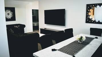 Un saló modern amb televisió de pantalla plana penjada a la paret, un sofà, una taula de centre amb un corredor de disseny blanc i negre, i una taula de dinar amb cadires.