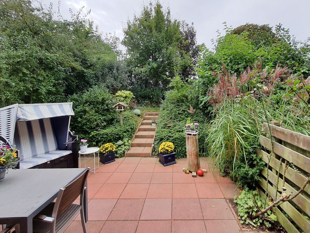 A garden patio with a table and chairs, a striped bench, and a wooden fence.